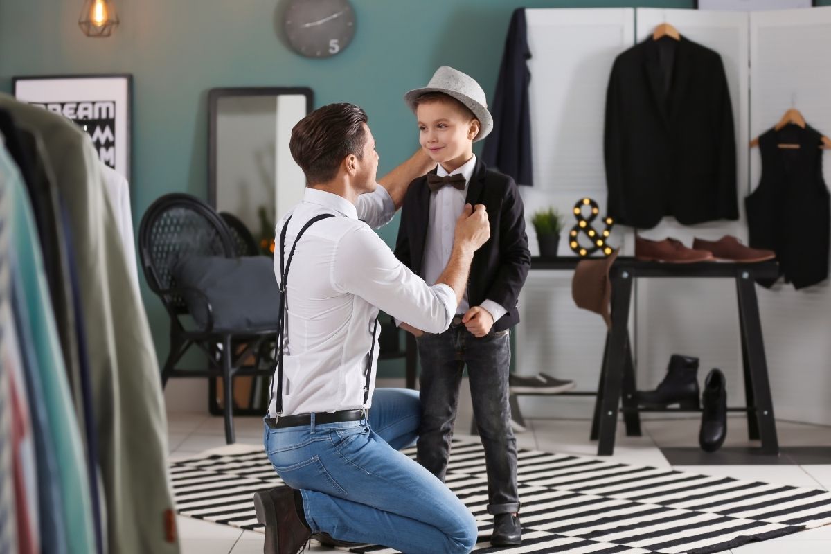 man wearing suspenders over a white longsleeves while fixing a kid's coat 