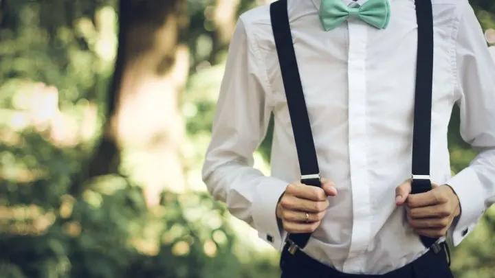 man wearing suspenders over a white longsleeves with a green bow tie