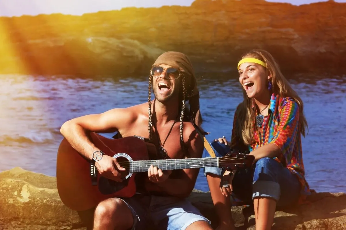 two Hippies, boy playing the guitar beside a girl singing by the sea