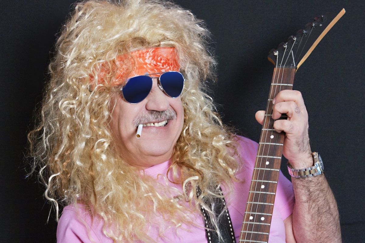 man wearing Notable Clothing In Rockers Of The 70s style such as blonde wig, headband, sunglasses, and electric guitar