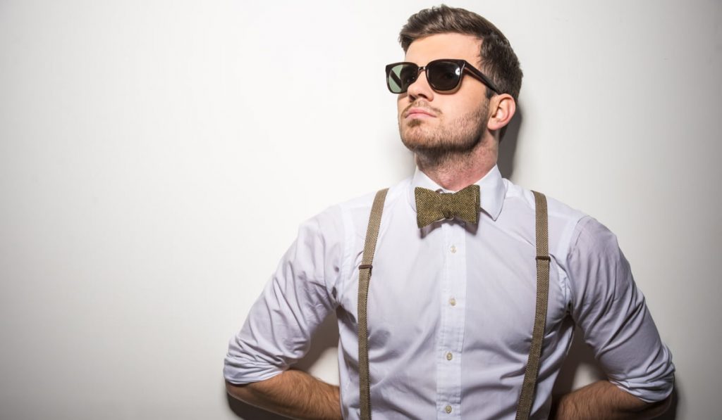 trendy young man wearing brown suspenders and a bow tie with sunglasses 