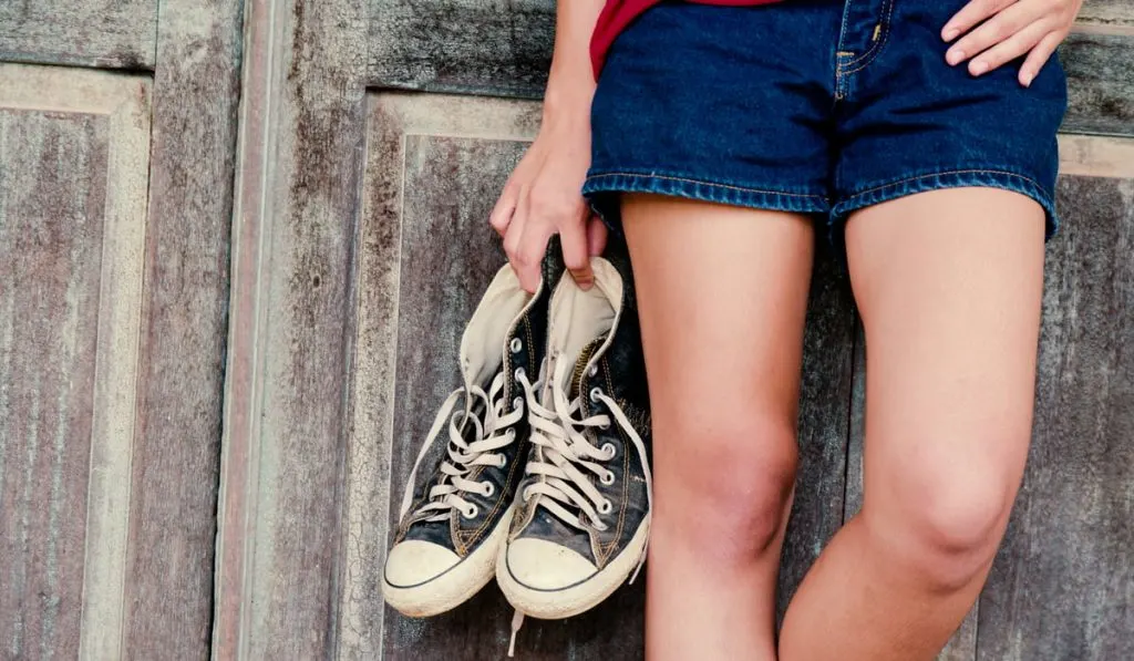 woman holding black converse shoes