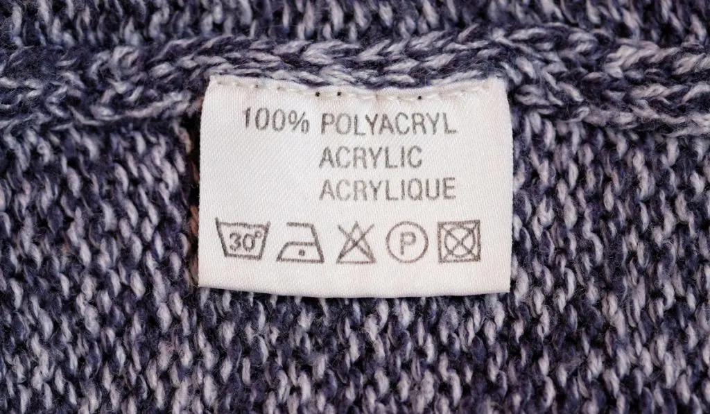 100% polyacryl (acrylic). Fabric composition white clothes label on blue texture background.