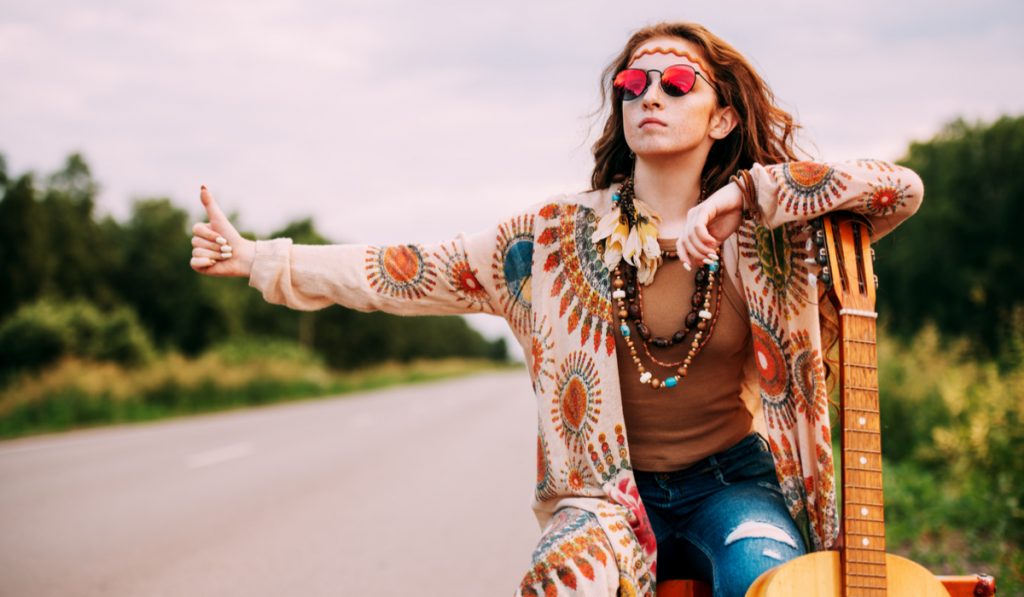 Beautiful hippie girl standing on a highway and catching a passing car.