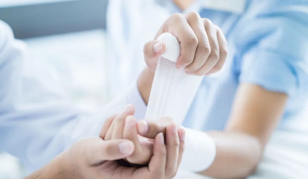 Close-up doctor is bandaging upper limb of patient.