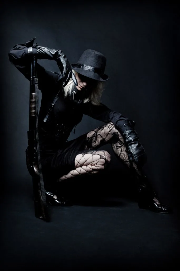 Gangster girl wearing fishnet stockings, black skirt,  fitted top, and a hat 