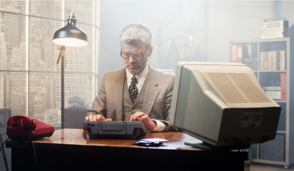Man in glasses sitting at old computer and examining diskettes at the table
