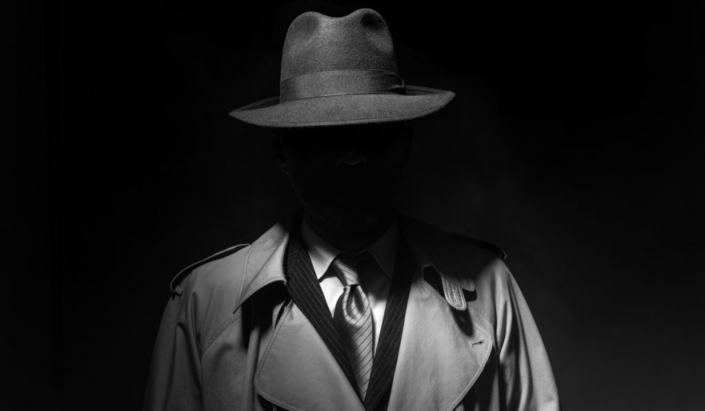 Man posing in the dark with a fedora hat and a trench coat