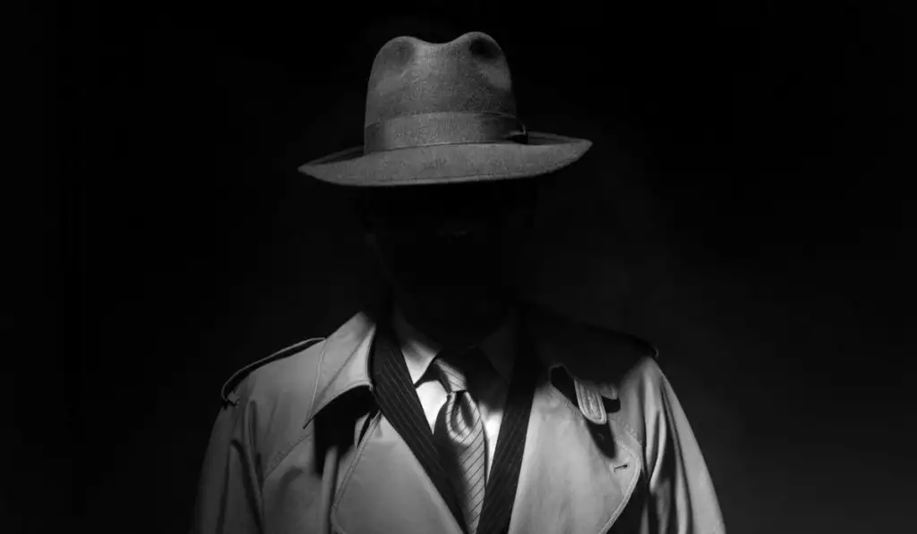 Man posing in the dark with a fedora hat and a trench coat