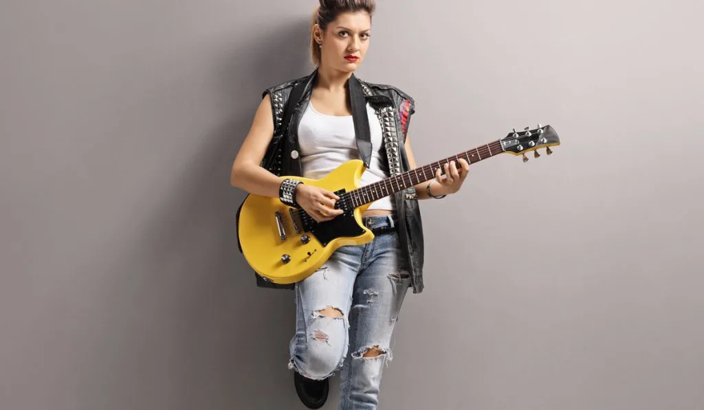 Punk girl playing an electric guitar and leaning against a wall