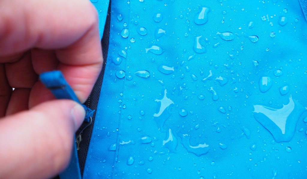 Selective focus of water drops on bright blue fabric and black zipper 