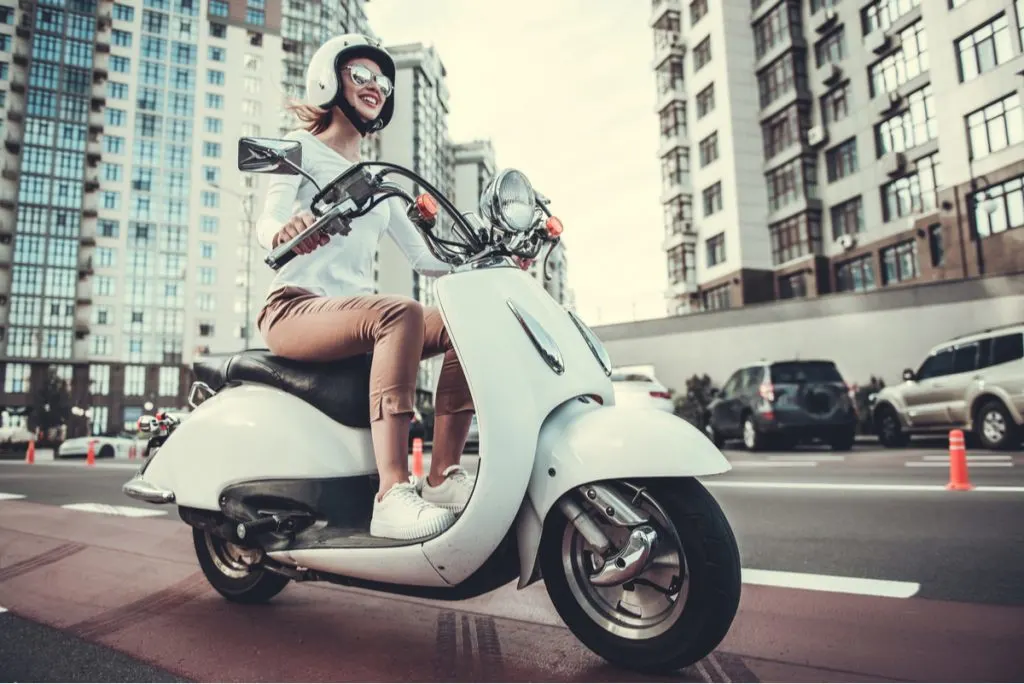 Smiling girl wearing shades  riding a scooter mods