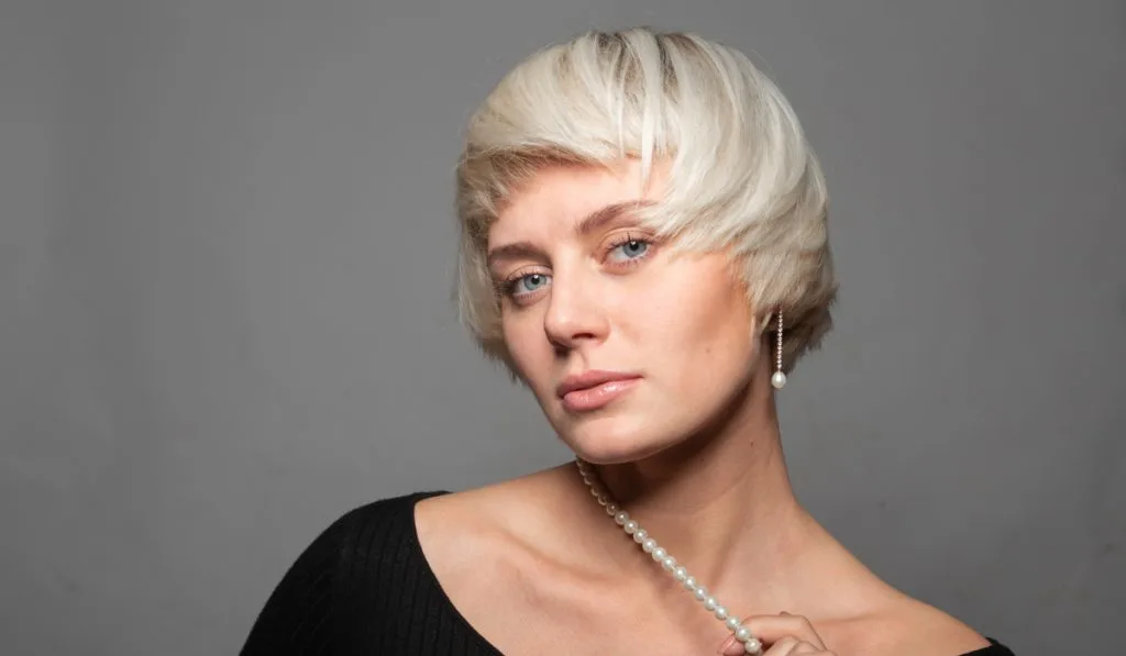 Studio portrait of a pretty blonde woman in a black dress and a necklace of white pearls,