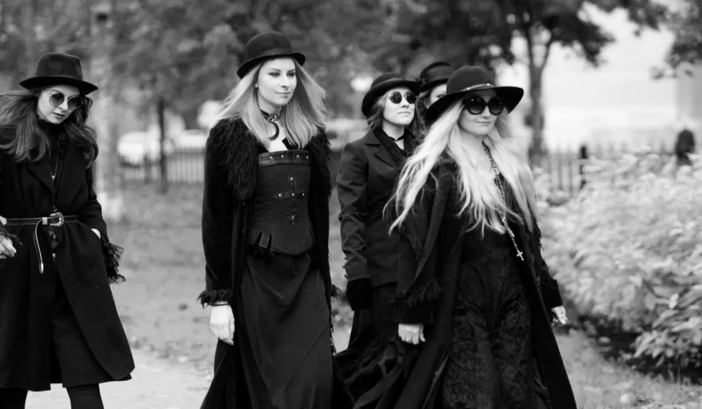  a group of witches or Goths in black clothes and hats go down the street