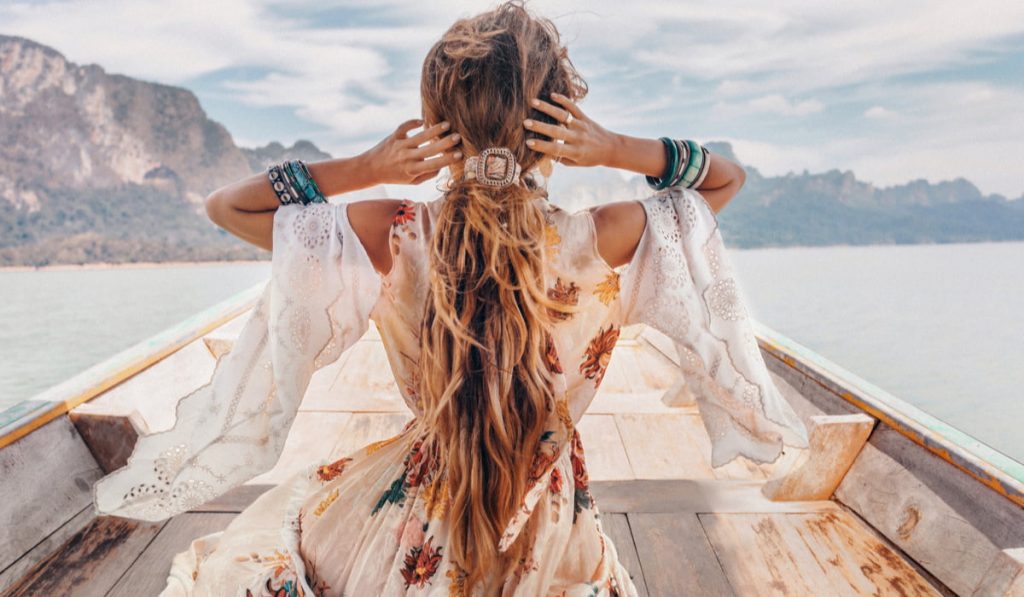 back view of a lady in bohemian style dress on a boat in the lake 