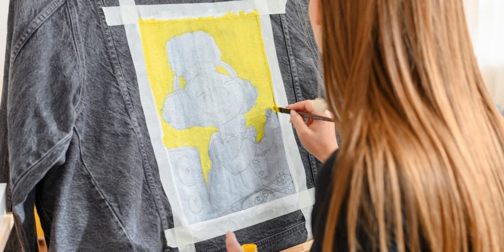 girl painting over pencil drawing on jean jacket