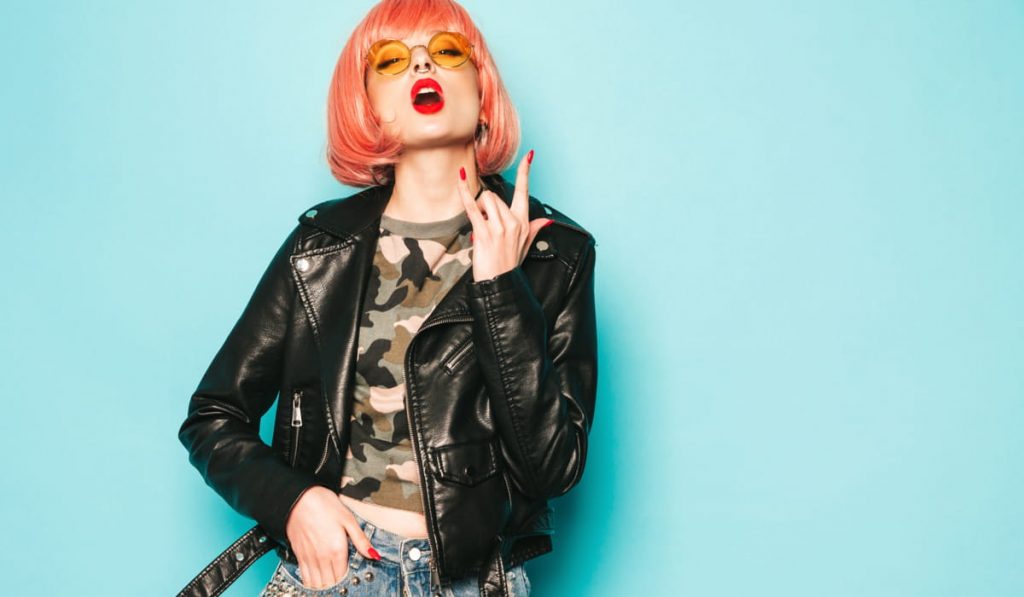 glam female rocker wearing a pink wig, yellow glasses, red lipstick and leather jacket