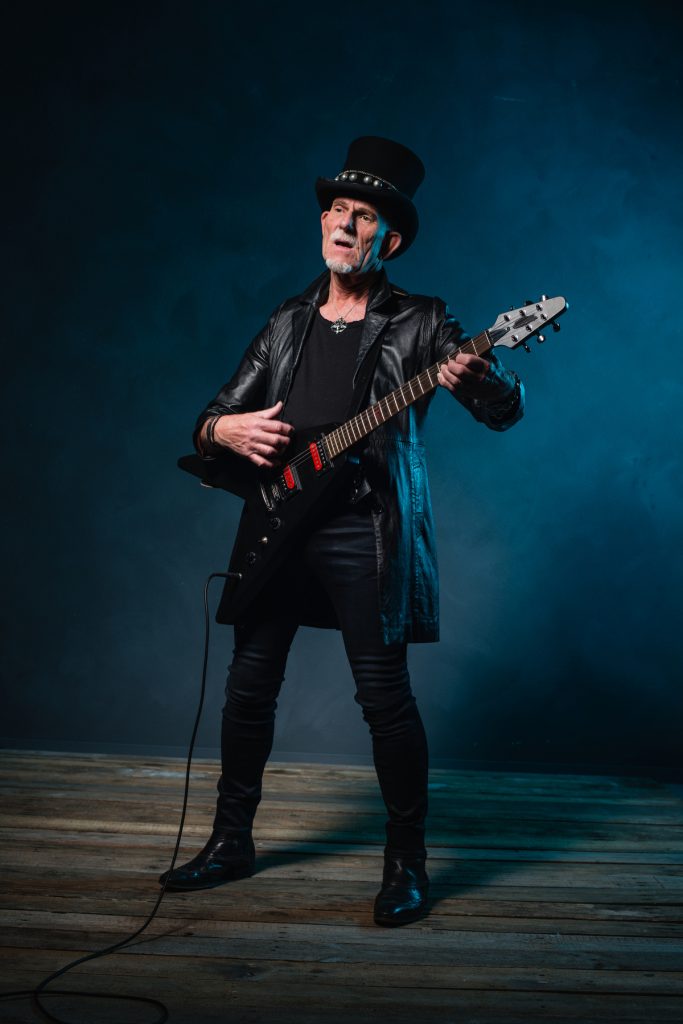 glam rocker male in tight jeans, t-shirt, and leather jacket playing an electric guitar