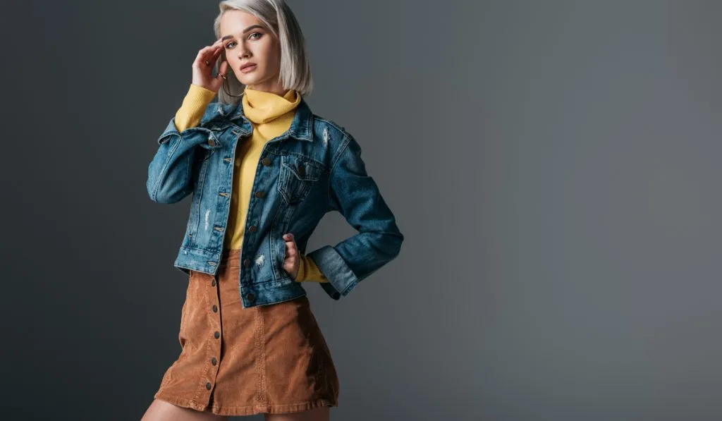 woman posing in yellow turtleneck, trendy corduroy skirt and jeans jacket, isolated on grey background