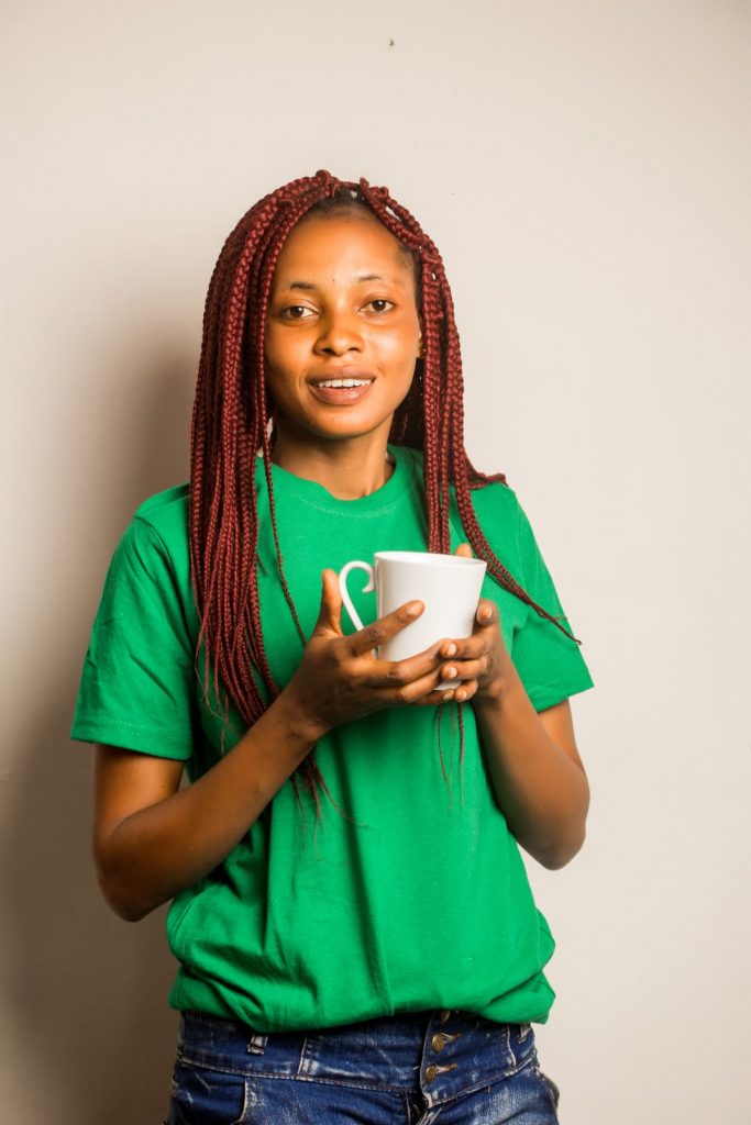 woman wearing loose fitting green shirt and stylish blue jeans drinking tea