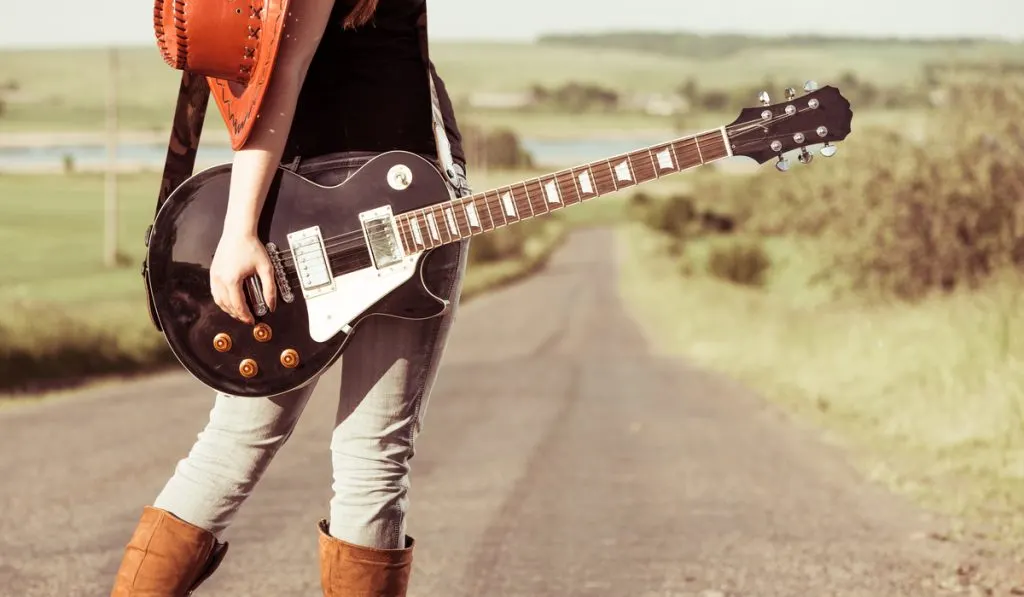 woman with guitar boots and hat on the road