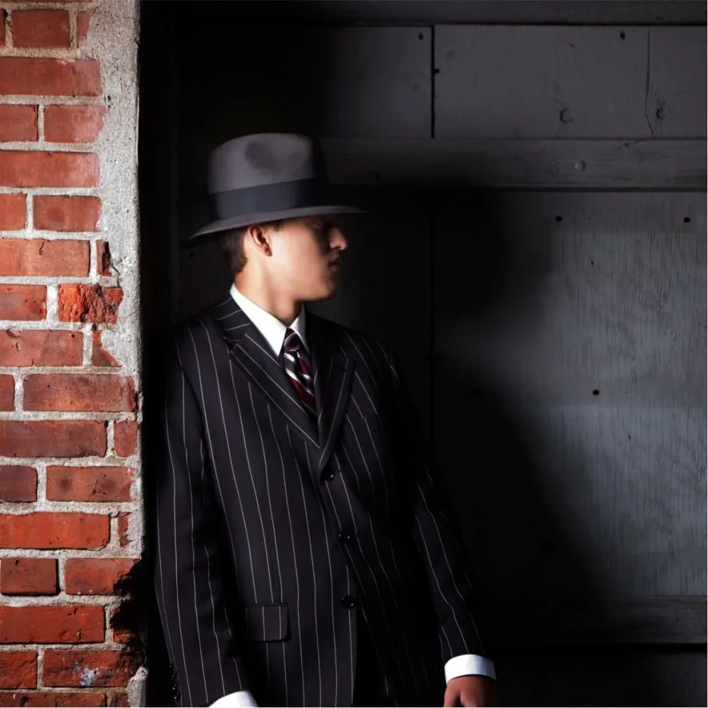 young man in pinstripe suit standing against a brick wall